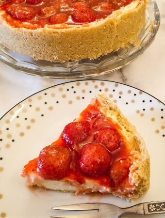 Strawberry cheesecake on a plate next to the whole cheesecake.