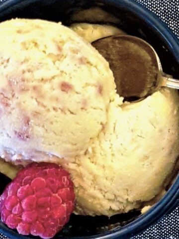 A scoop of homemade raspberry ripple ice cream in a dish with a raspberry.