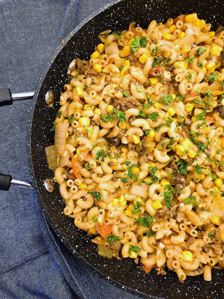 Closeup of a black frying pan containing a finished dish of American goulash and corn.