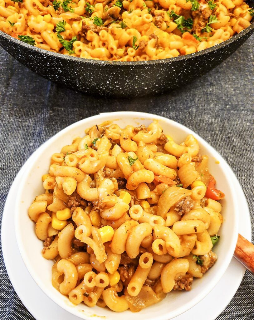 American goulash in a dish in front of the pan of goulash.