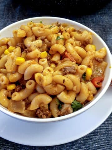 Close up of a white bowl of goulash with a frying pan in the background.