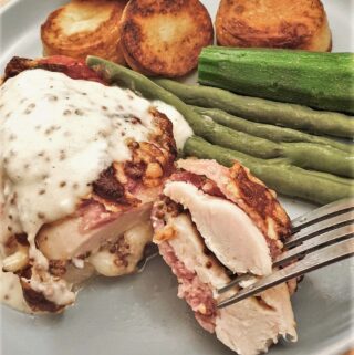 A bacon-wrapped chicken parcel on a plate with vegetables and potatoes.