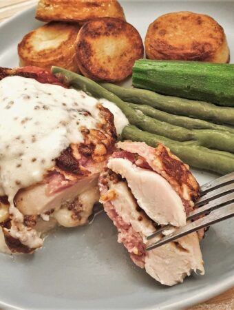 A bacon-wrapped chicken parcel on a plate with vegetables and potatoes.