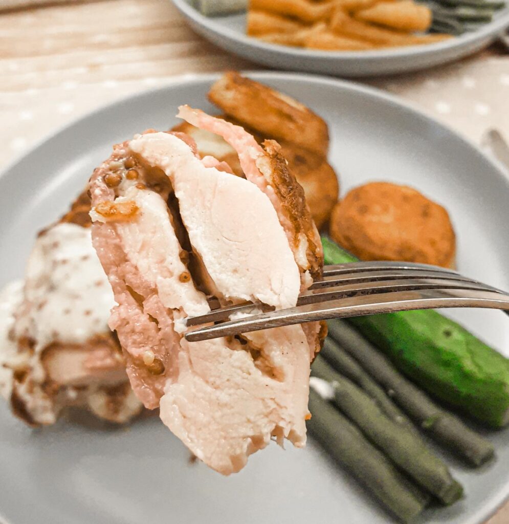 A slice of bacon-wrapped chicken on a fork showing the juiciness.