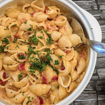 A dish of cheesy barbeque pasta sprinkled with chopped parsley.