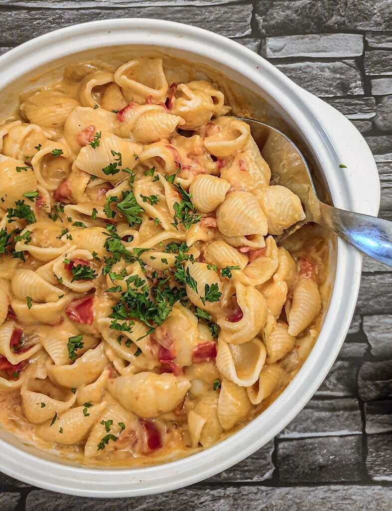 A dish of cheesy barbeque pasta sprinkled with chopped parsley.