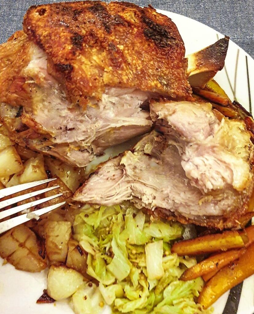 A crispy eisbein on a plate with vegetables, showing the inside of the meat.