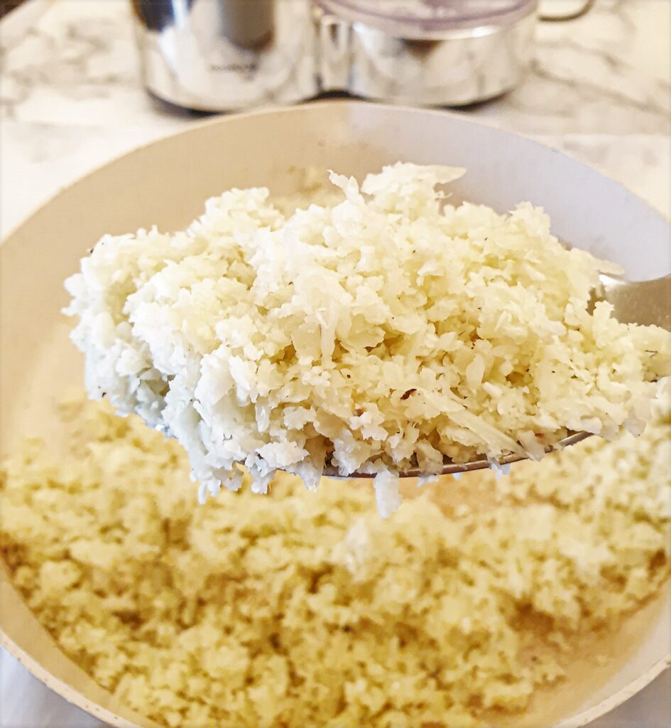 A spoonful of cauliflower rice held over the serving dish.