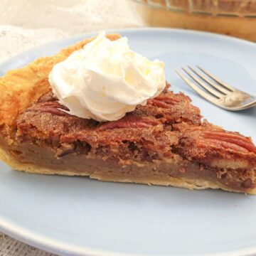 A slice of pecan nut pie, topped with cream, on a plate with a fork.