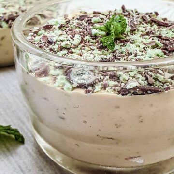 A glass dish filled with peppermint crisp fridge tart, topped with a sprig of mint.