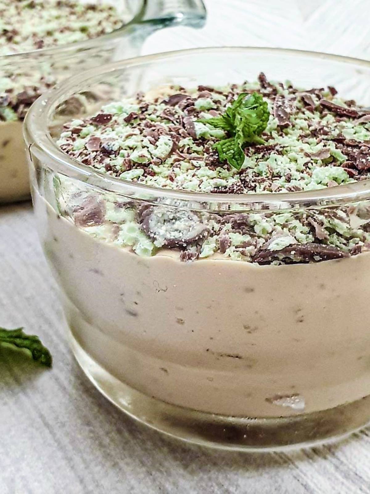 A glass dish filled with peppermint crisp fridge tart, topped with a sprig of mint.