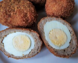 Four scotch eggs with one of them cut in half to show the inside.