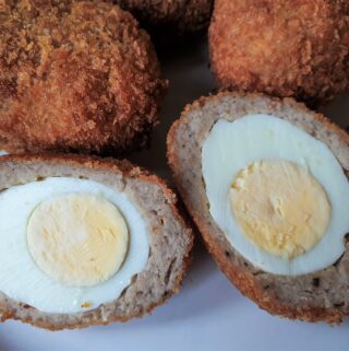 Four scotch eggs with one of them cut in half to show the inside.