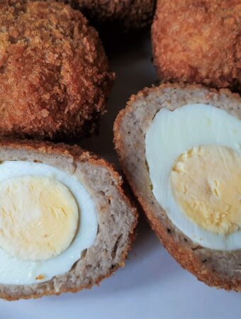 Four scotch eggs with one of them cut in half to show the inside.