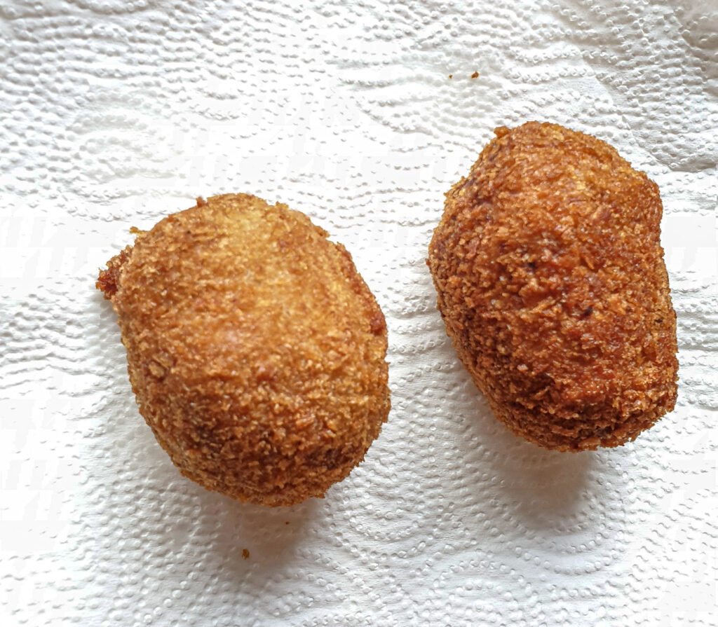 Two deep-fried scotch eggs draining on a paper towel.