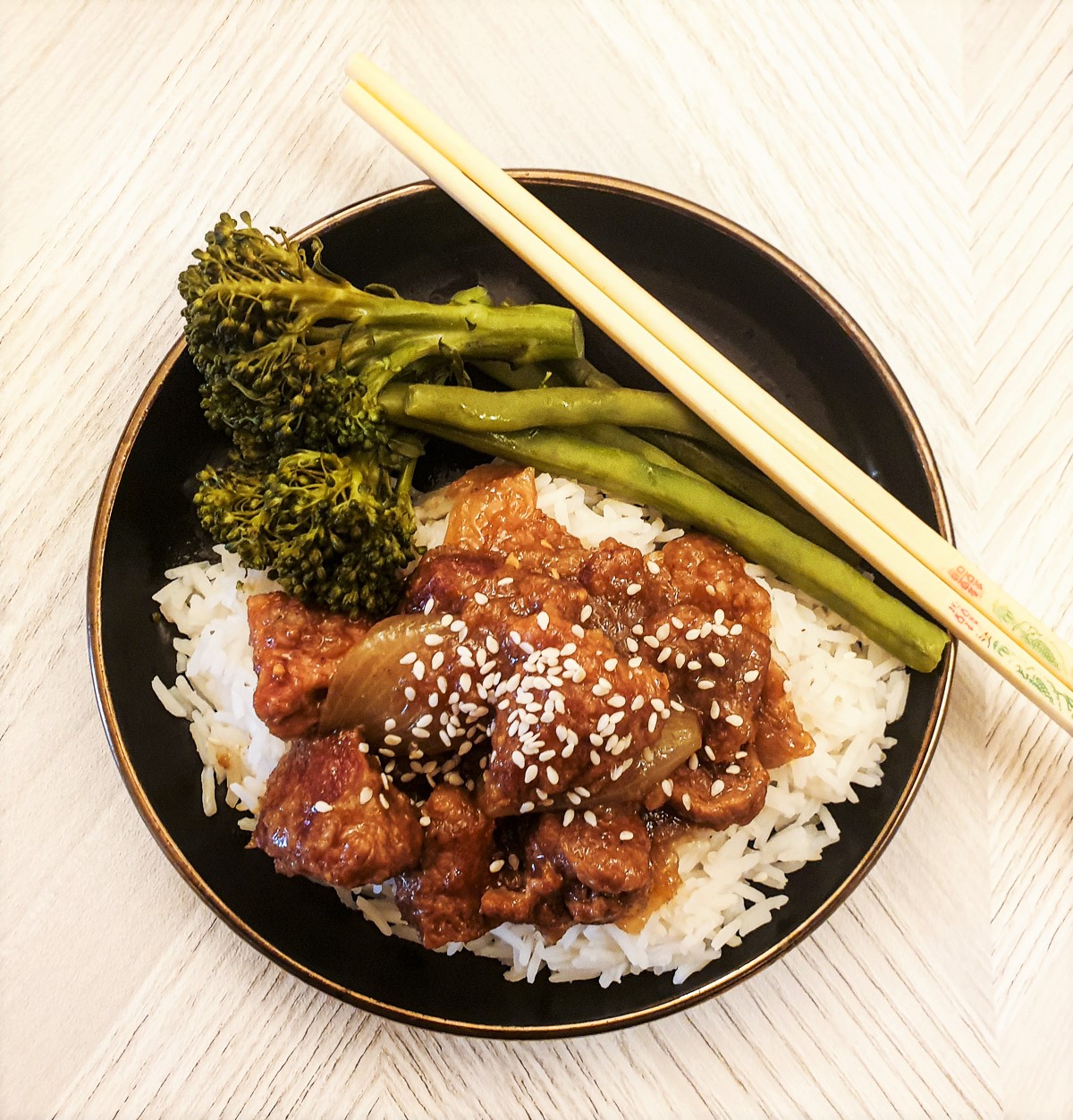 Overhead shot of a plate of sticky Asian pork on a bed of rice, with vegetables.