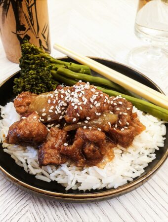 Sticky asian pork on a pile of rice, sprinkled with sesame seeds.