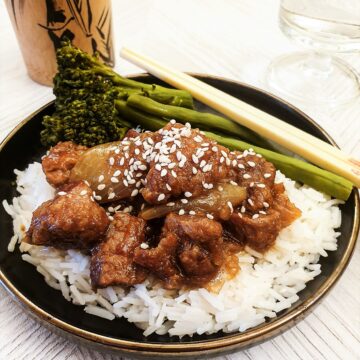 Sticky asian pork on a pile of rice, sprinkled with sesame seeds.