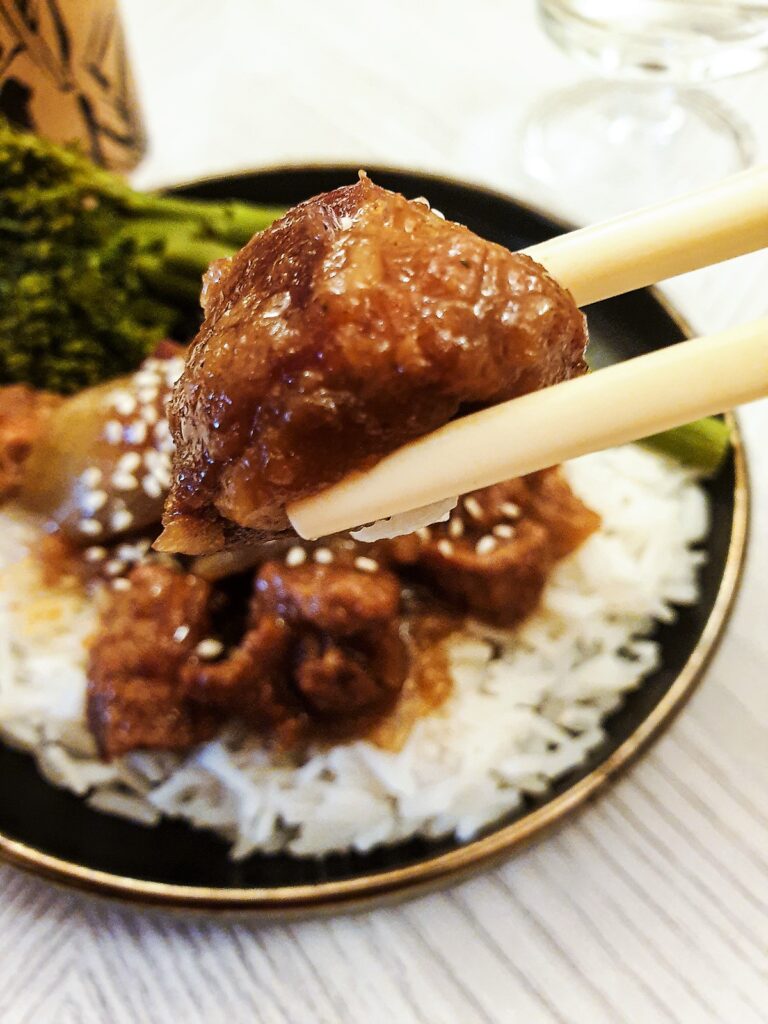 Close up of a piece of Asian pork held in chopsticks.