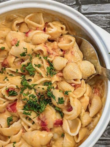 A dish of cheesy barbeque pasta sprinkled with chopped parsley.