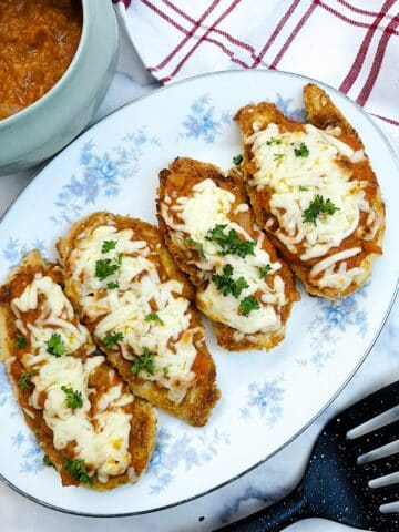 Four slices of cheese-topped crispy chicken parmesan on a blue-flowered platter.