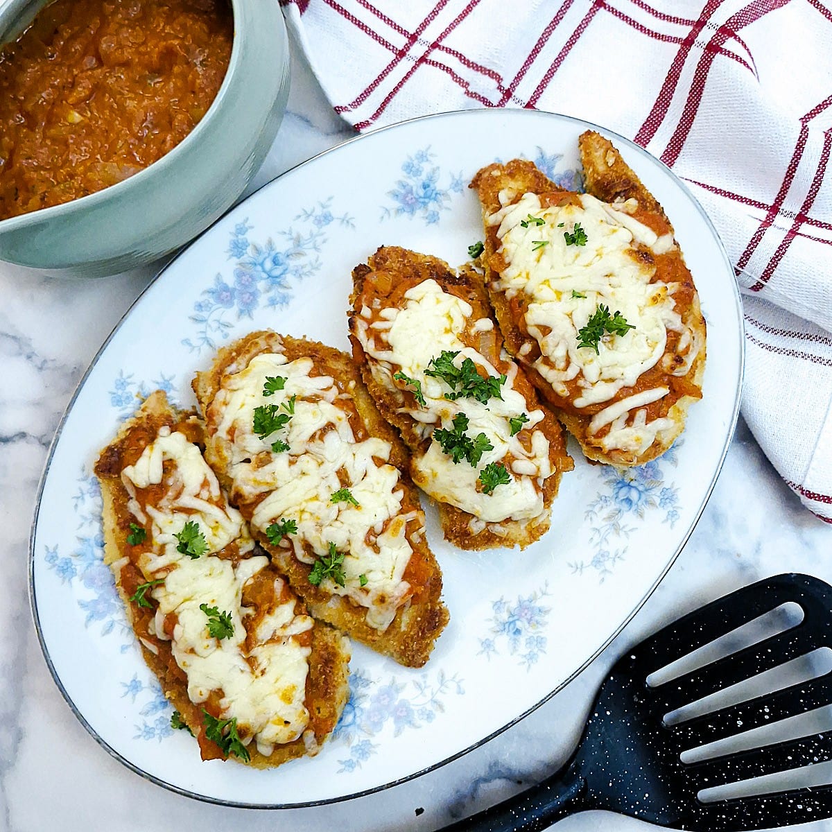 Four slices of cheese-topped crispy chicken parmesan on a blue-flowered platter.