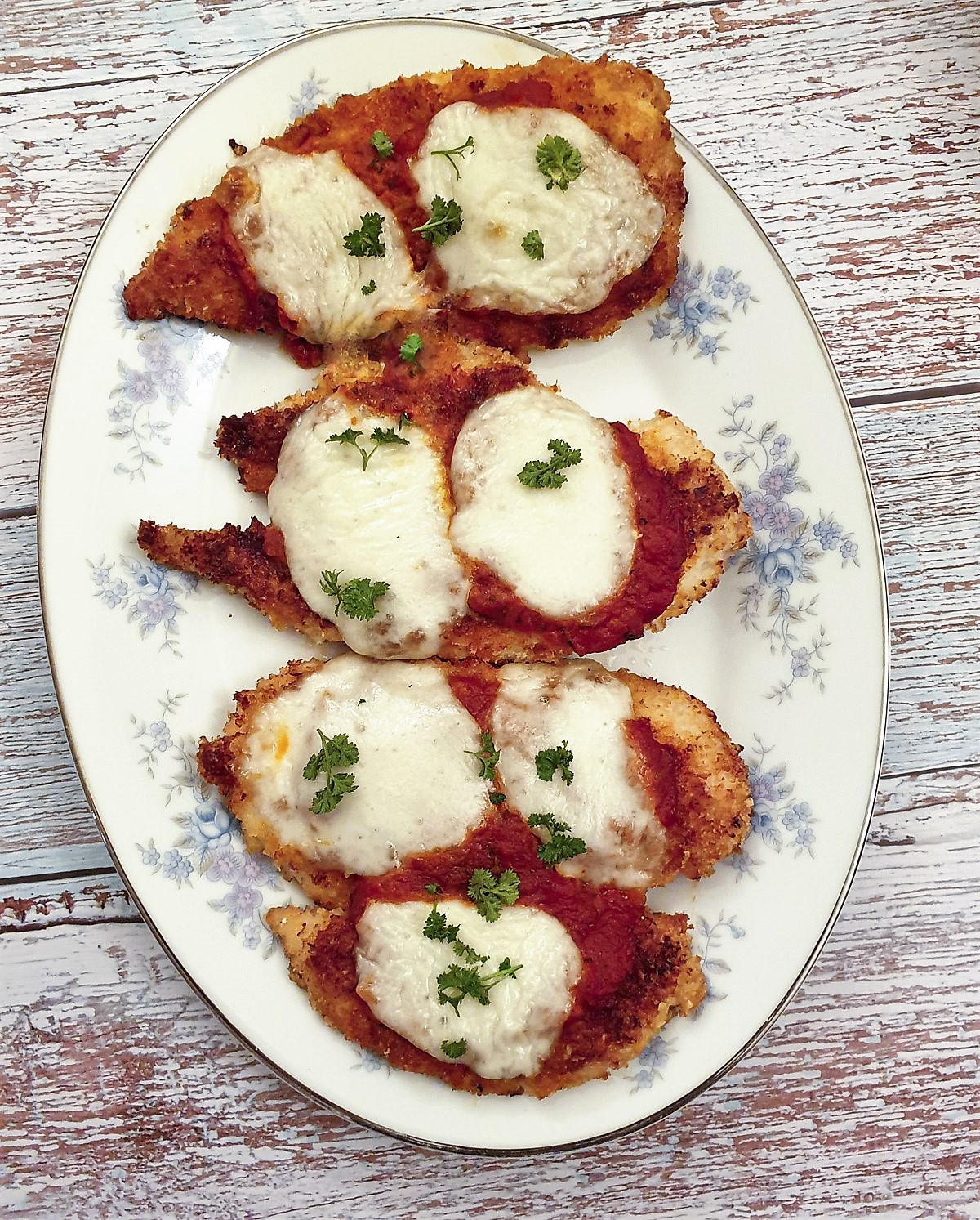 Four helpings of chicken parmesan on a plate.