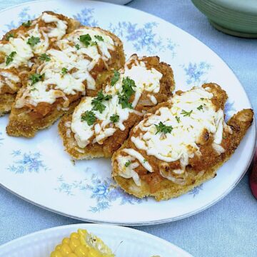 4 pieces of parmesan chicken topped with melted mozzarella on a platter, surrounded by dishes of vegetables.