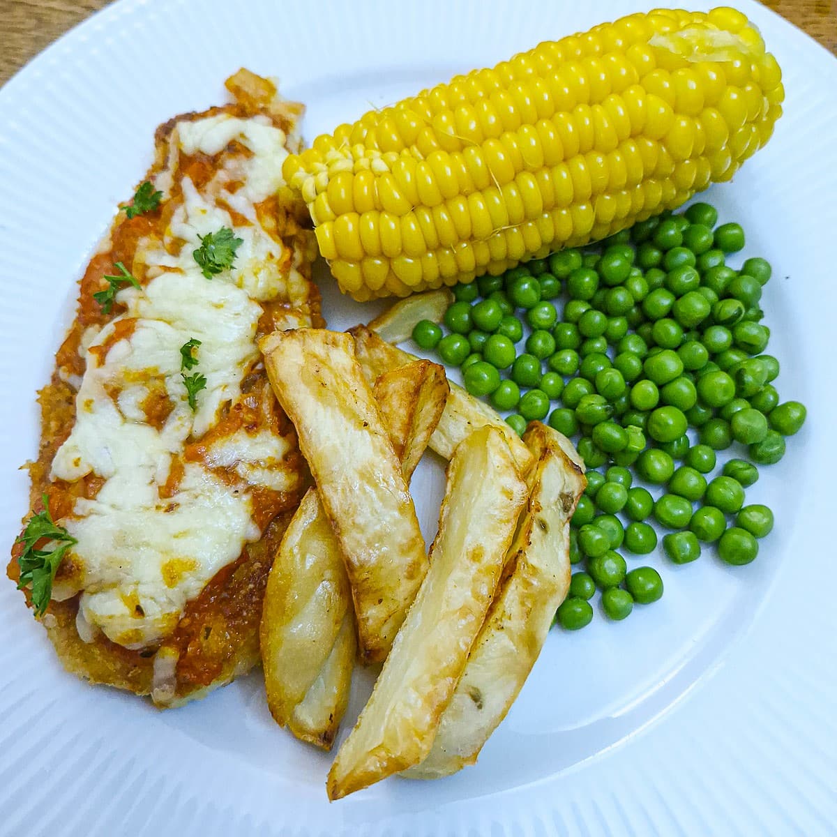 Chicken parmesan of a plate with chips and vegetables.