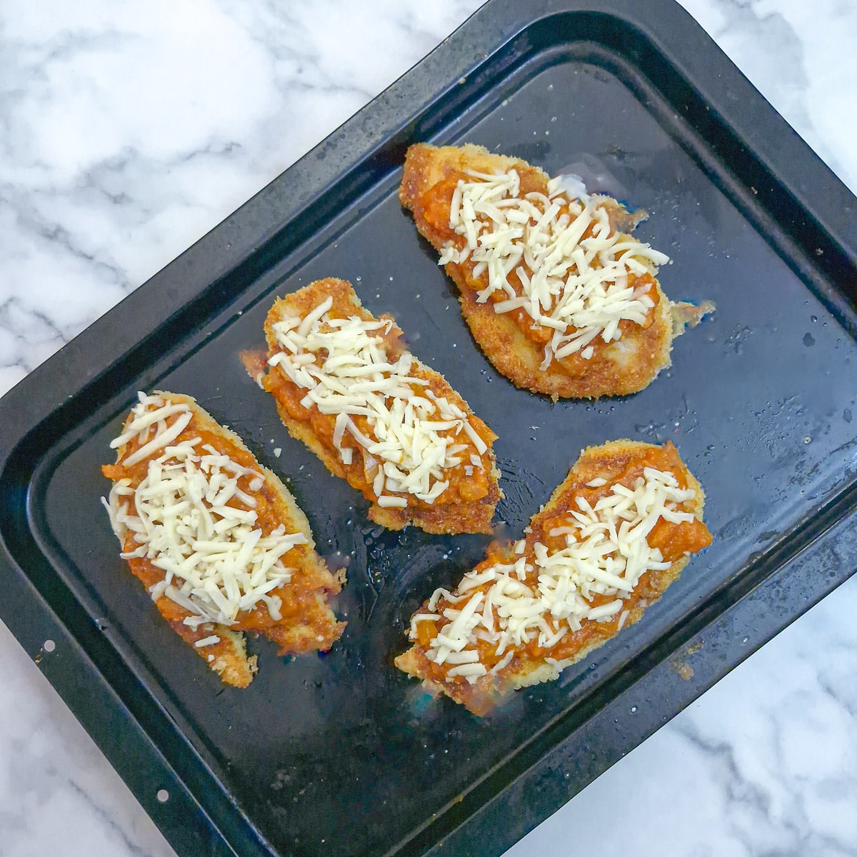 Step 8 - 4 pieces of crumbed chicken topped with marinara sauce and grated mozszarella on baking tray.