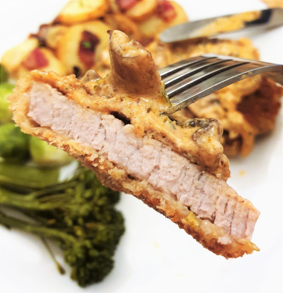 A slice of crispy beef schnitzel on a fork, showing how the coating adheres to the meat.