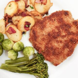 A crispy crumbed beef schnitzel on a plate next to a pile of German fried potatoes.