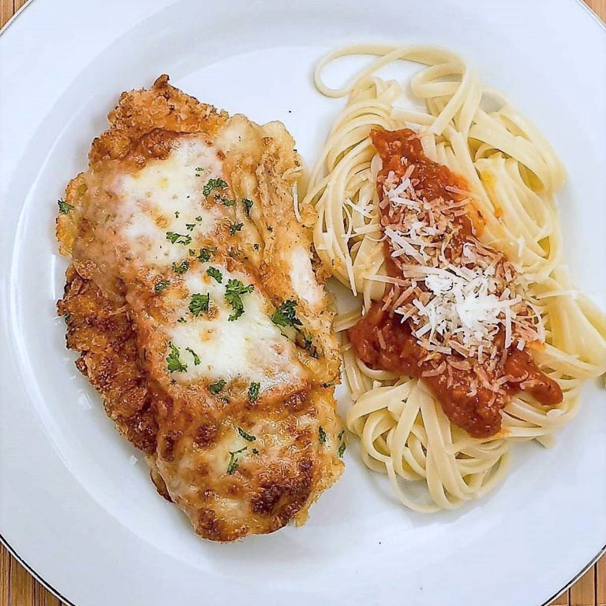Chicken parmesan on a plate with spaghetti topped with marinara sauce.