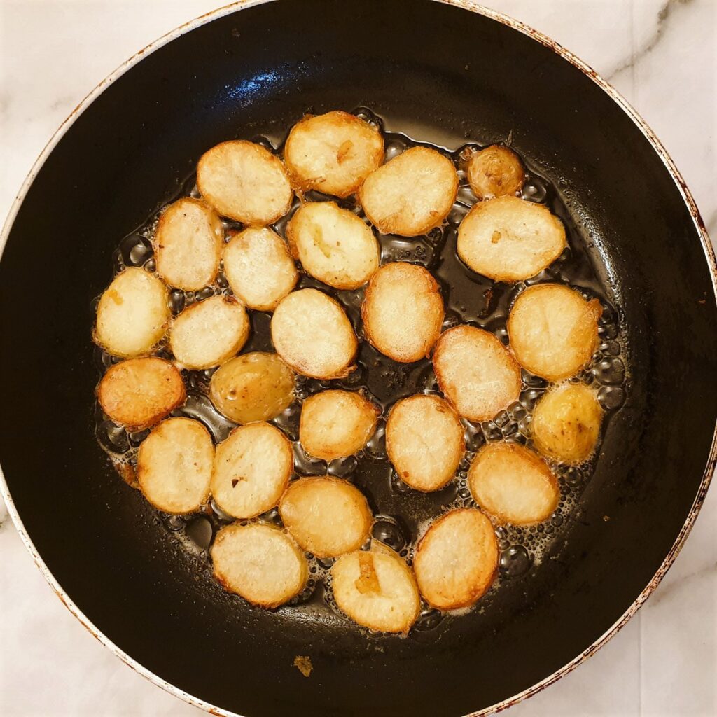 Slices of potatoes frying in a frying pan showing how they brown.