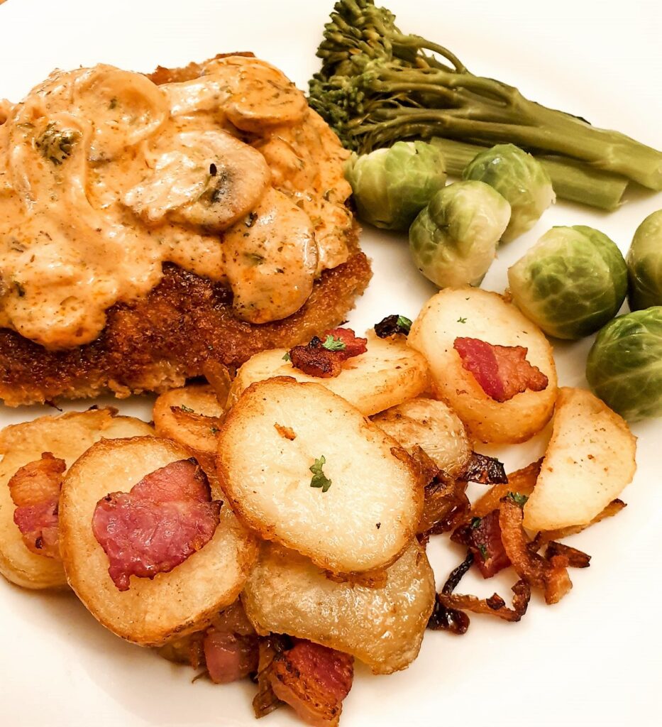 A plate of German fried potatoes served alongside a crispy beef schnitzel and mushroom sauce.