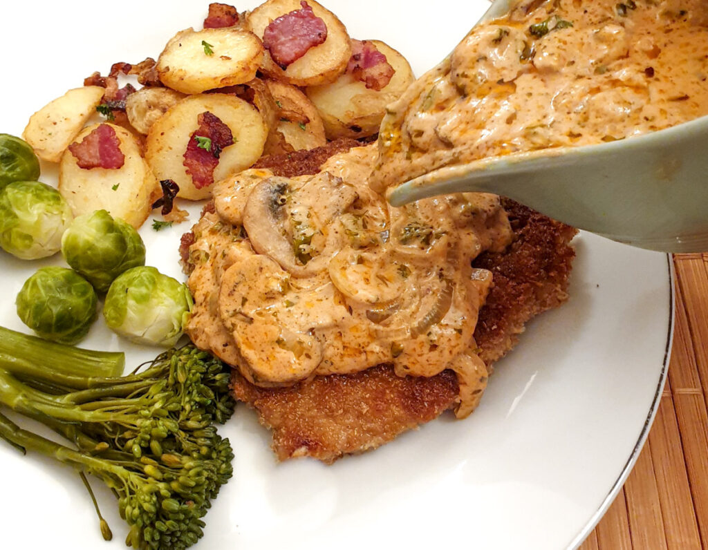 A helping of hunters sauce being poured over a schnitzel on a plate.