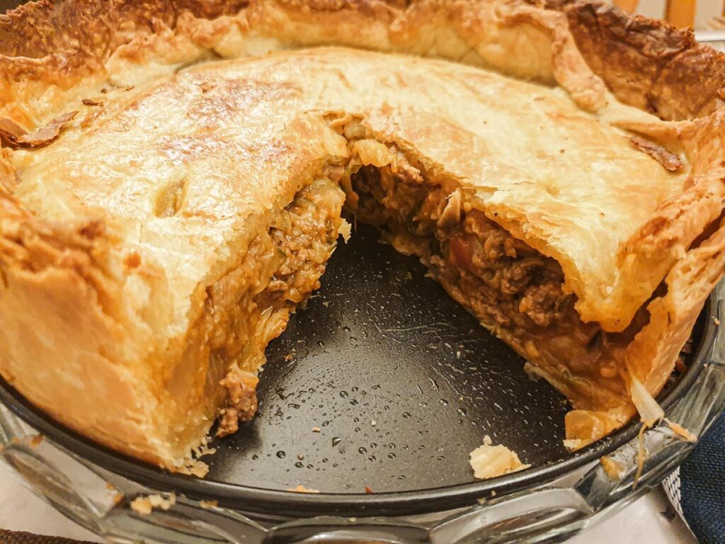 A beef and onion pie with one slice removed to show the filling.