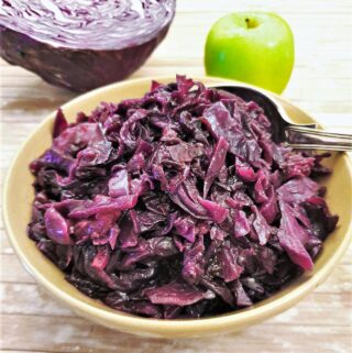A dish of spicy braised red cabbage with an apple and raw red cabbage in the background.