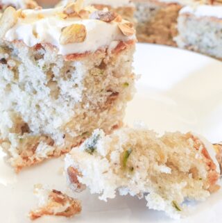 A slice of zucchini and pistachio cake with cream cheese frosting on a plate with a cake fork.