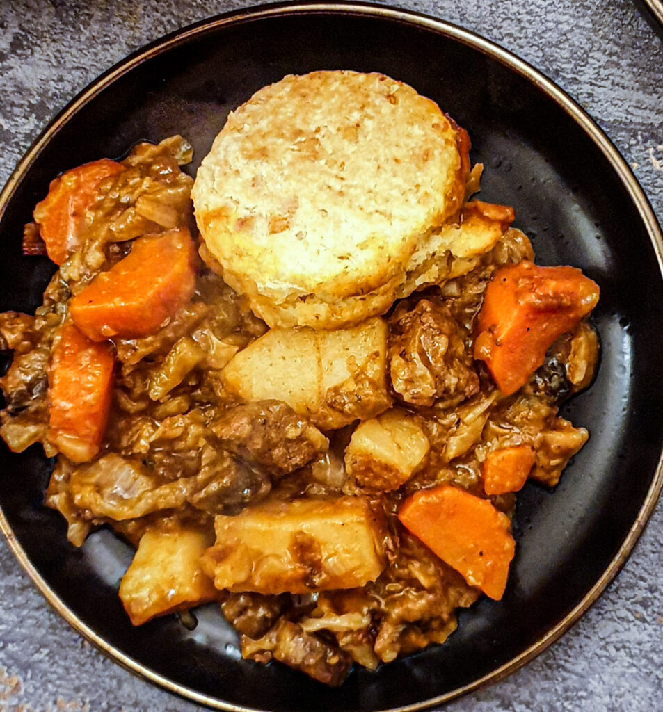 Close up of a plate of beef stew with  cheesy cobbler on the side.