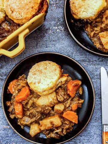 Overhead of a black plate of beef cobbler, with the corner of the serving dish in the background.