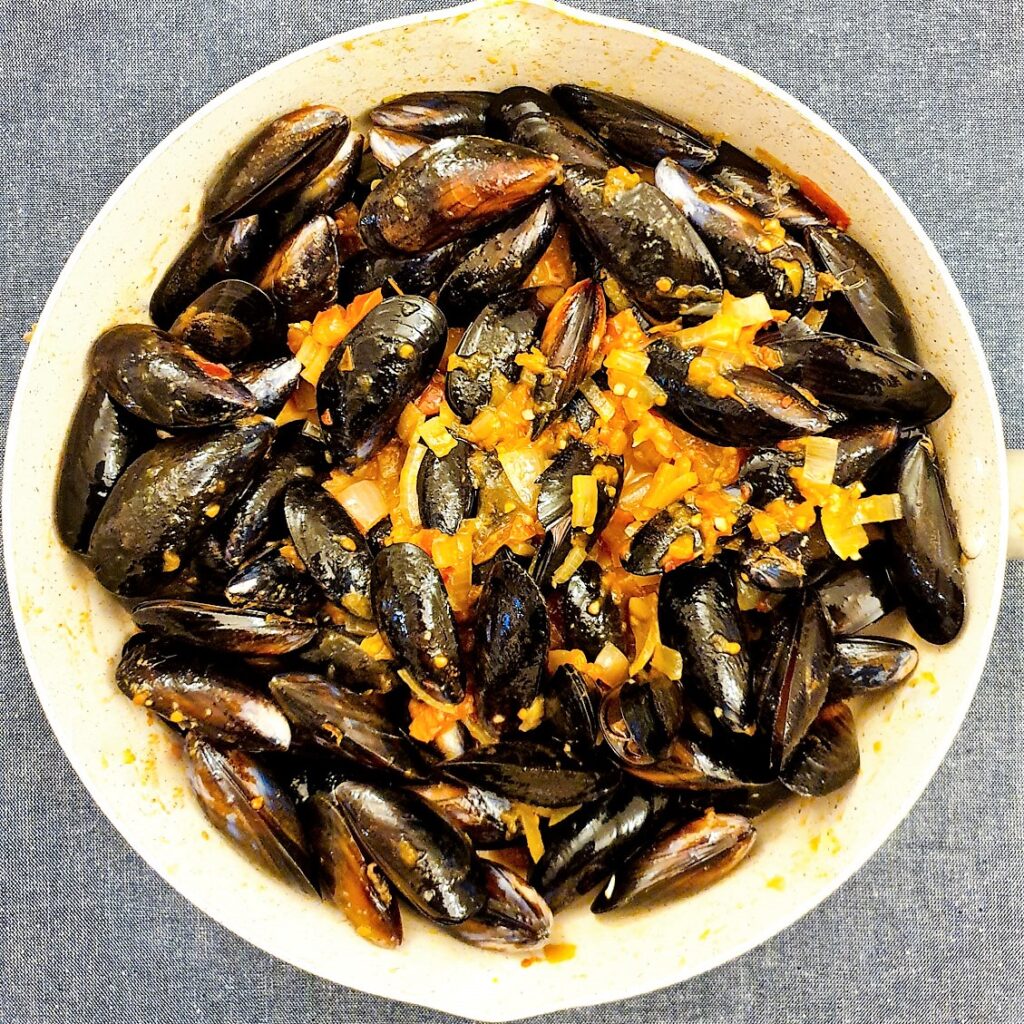 Fresh mussels in a pan mixed with tomato and onion sauce.