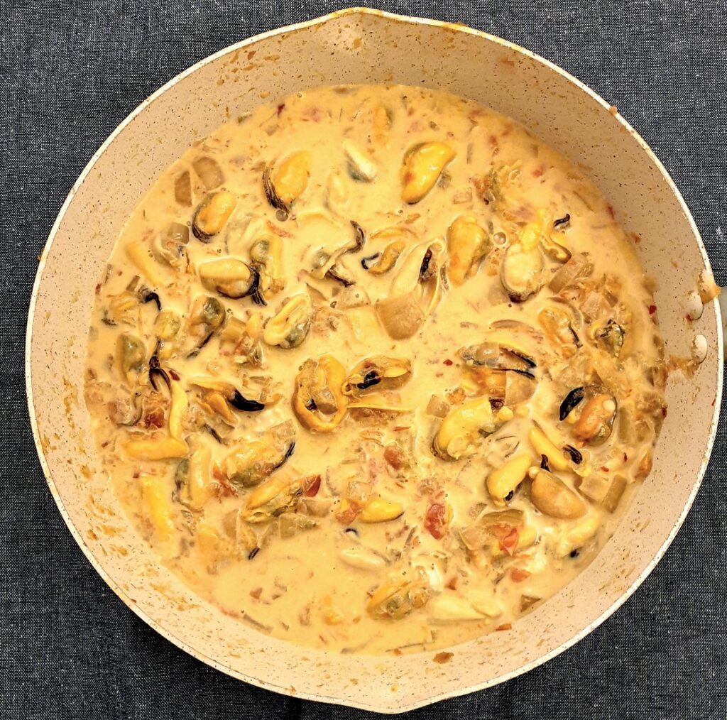 A pan of fresh mussels that have been removed from their shells, in a pan with cream and tomato sauce.