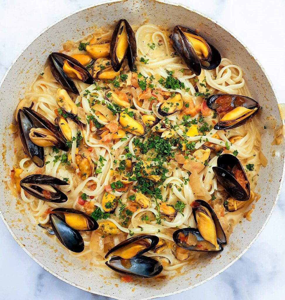 Overhead shot of a pan of fresh mussels in a spicy tomato and onion sauce, served with linguine.