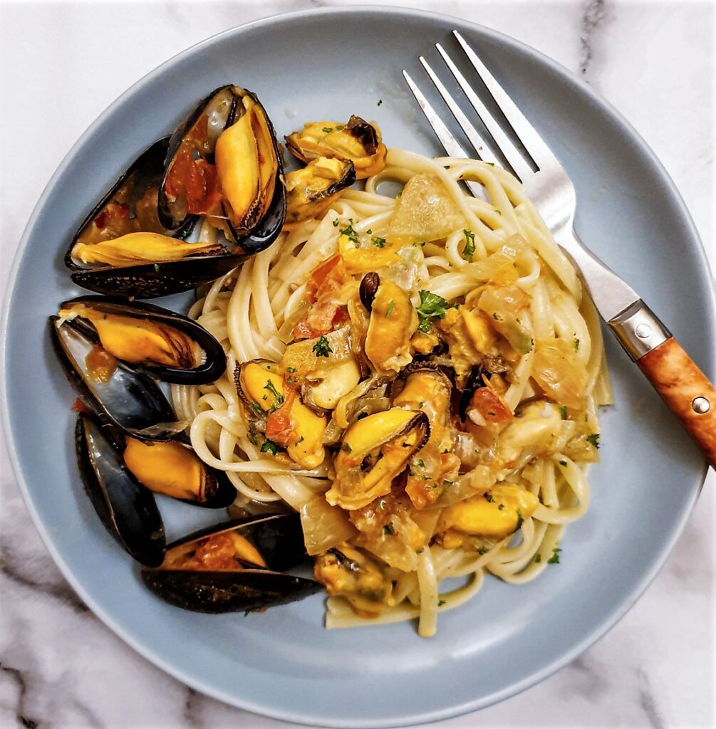 A plate of mussels with pasta, garnished with mussels in their shells.