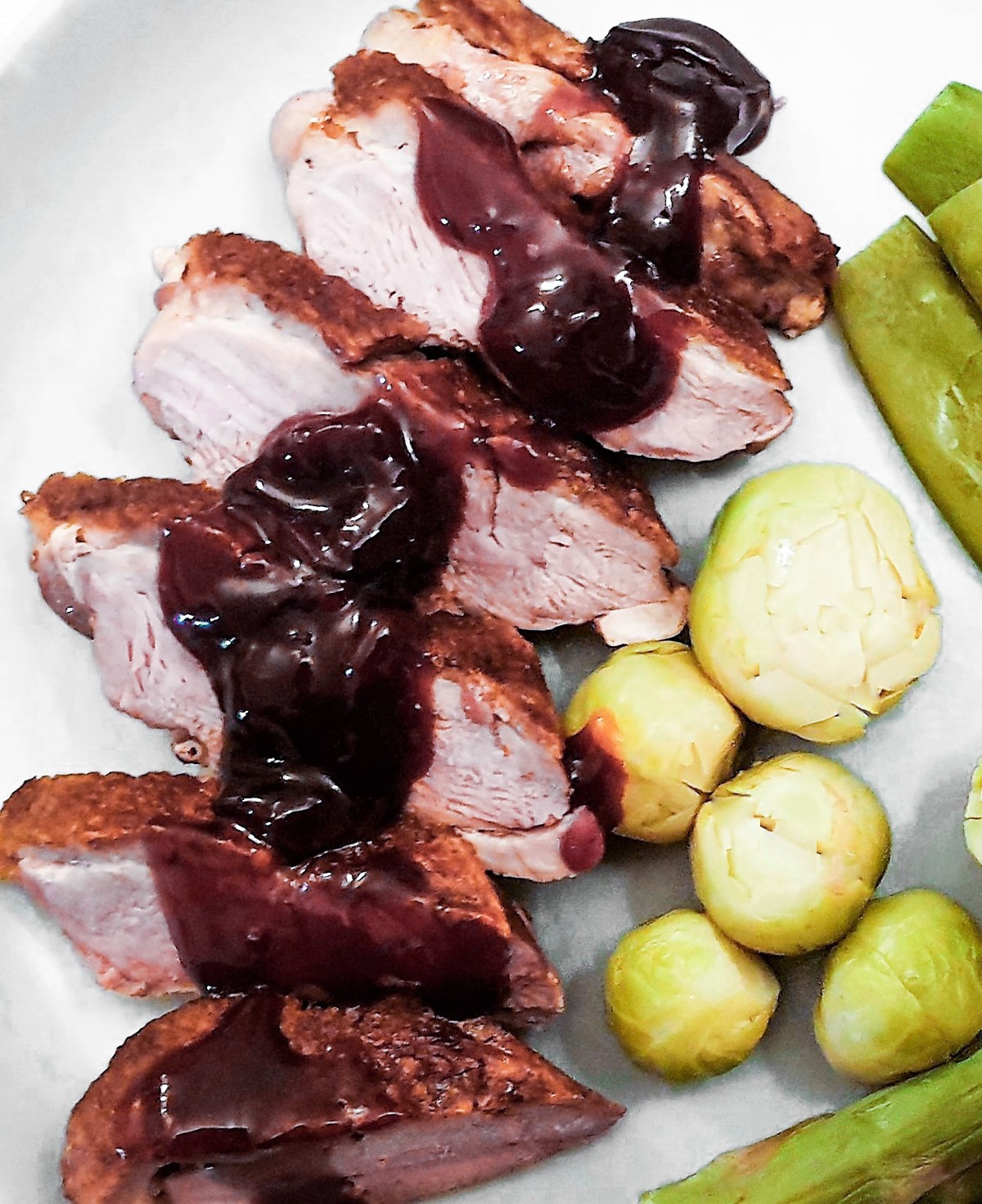 Slices of crispy roast duck covered with cherry sauce on a plate with vegetables.