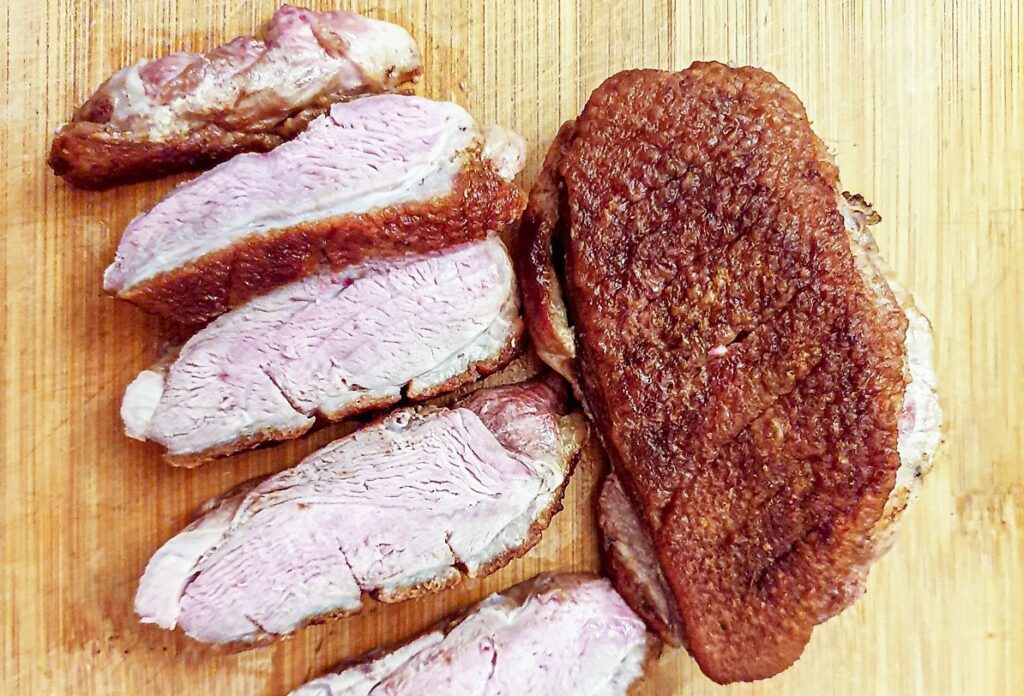 A duck breast cut into slices each with a piece of crispy skin.
