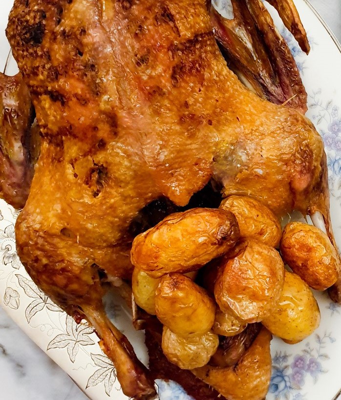 A roast duck with roast potatoes, showing the crispy skin.