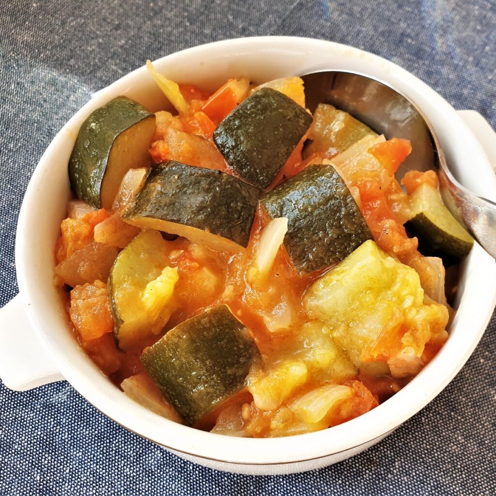 Close up of a dish of baby marrow with tomato and onions.