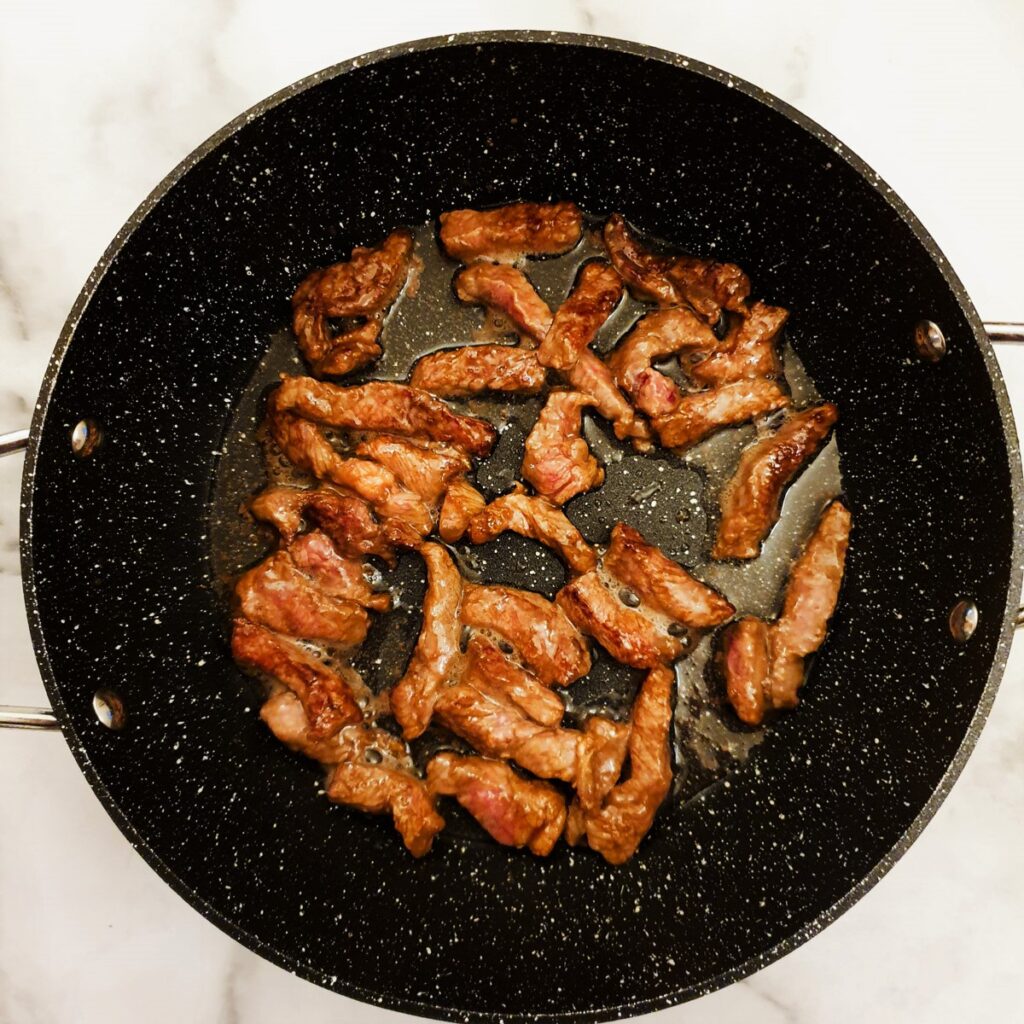 Slices of beef browning in a frying pan.